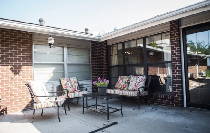 A cozy patio area with cushioned outdoor furniture, including chairs and a table, set against a backdrop of windows.