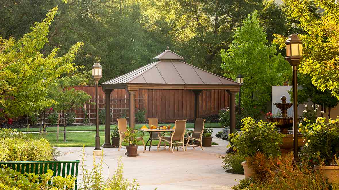 A serene backyard scene featuring a gazebo with patio furniture surrounded by lush greenery.