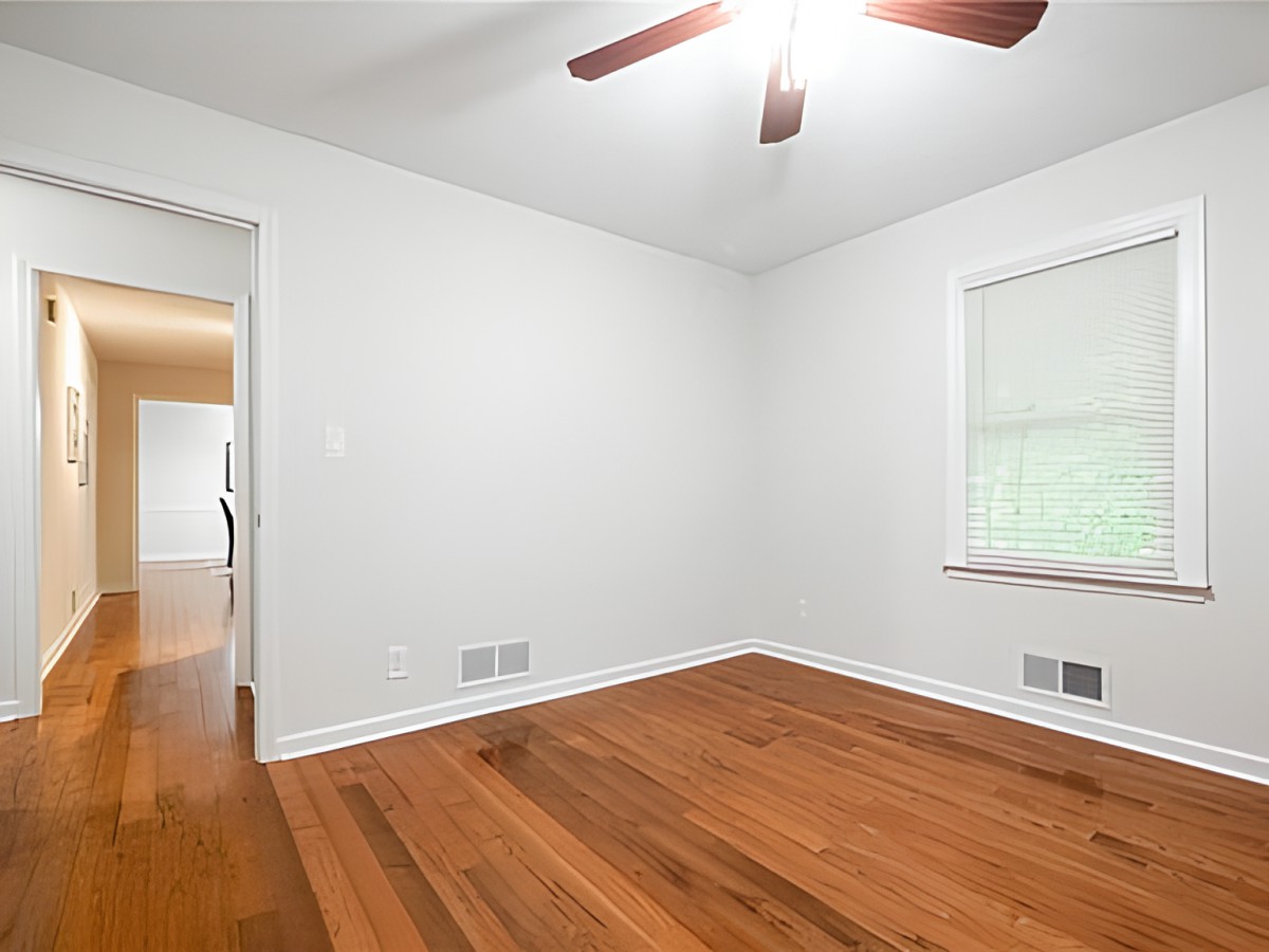 An empty room with hardwood floors, white walls, and a ceiling fan.