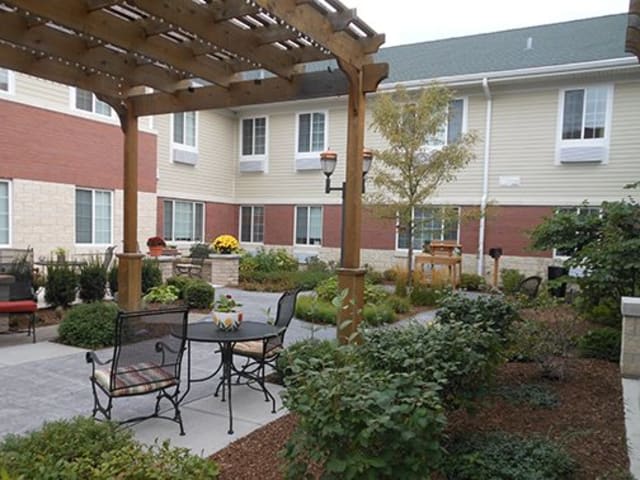 A cozy outdoor patio area with a pergola and seating, surrounded by lush landscaping in front of a building.