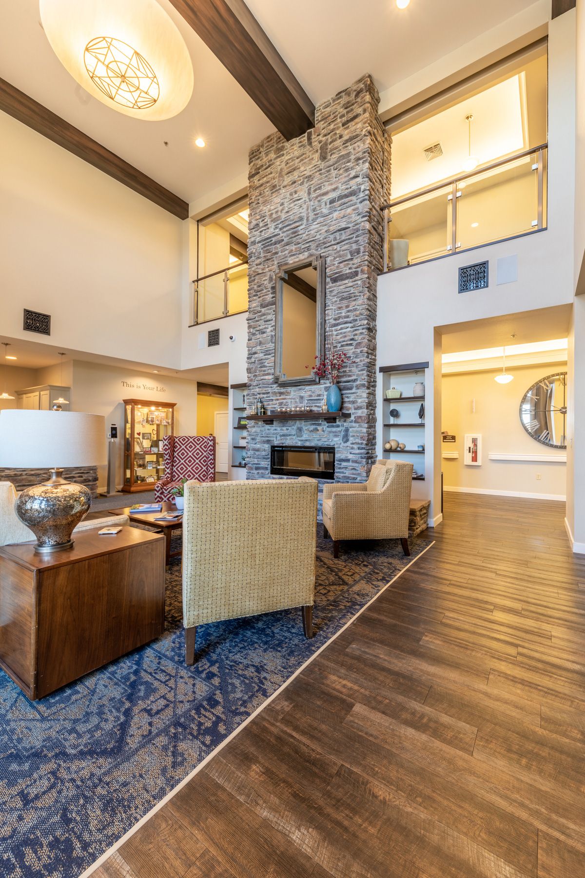 A modern, luxurious living room with a fireplace and high ceiling, featuring elegant furniture and wood flooring.