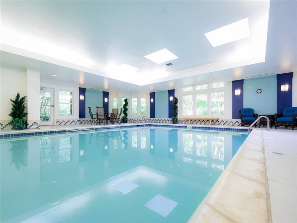 A modern indoor swimming pool with large windows and bright lighting.