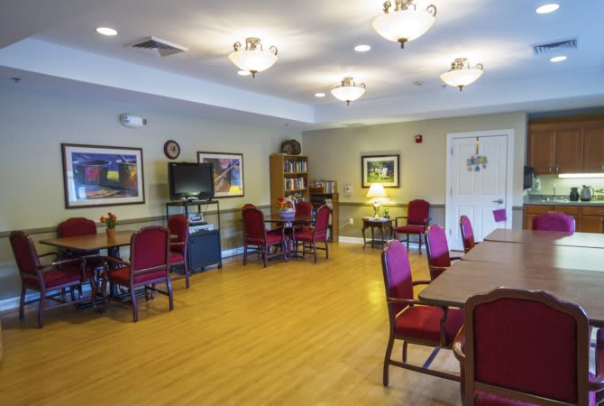 A well-lit room with tables and chairs, featuring a television and a bookshelf.