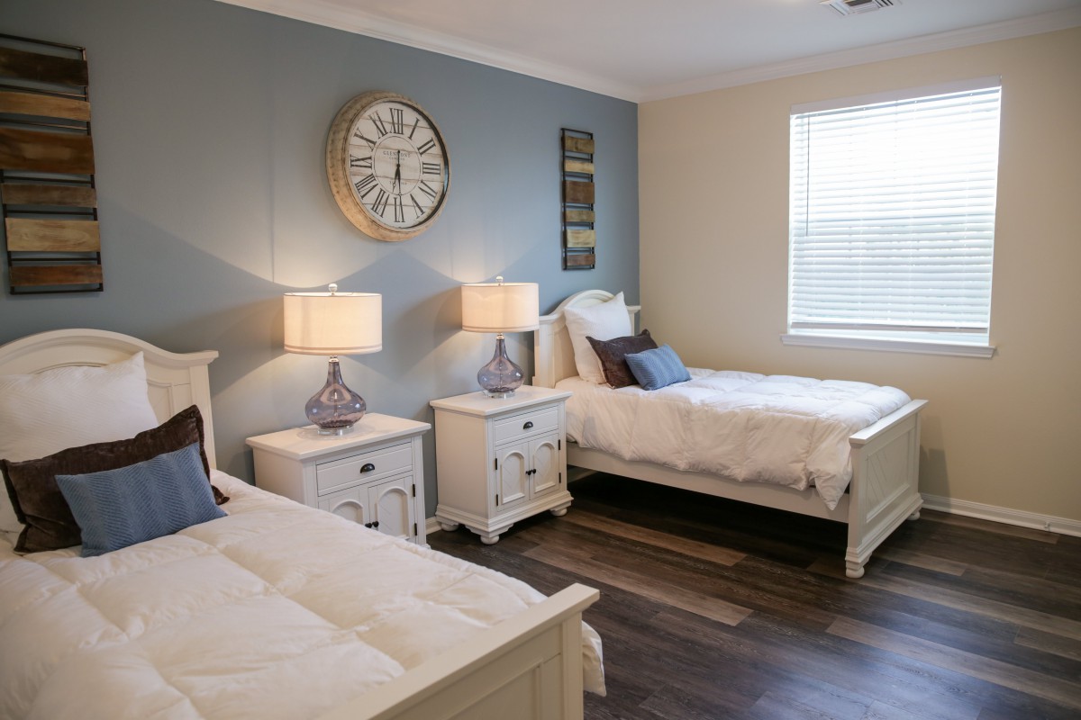 A cozy bedroom featuring two twin beds with matching nightstands and lamps, complemented by a large wall clock and decorative elements.