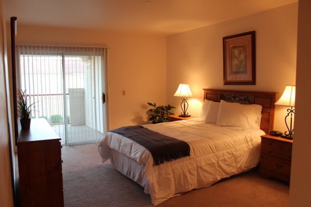 A cozy bedroom with a neatly made bed, bedside lamp, and sliding door leading to an outdoor area.