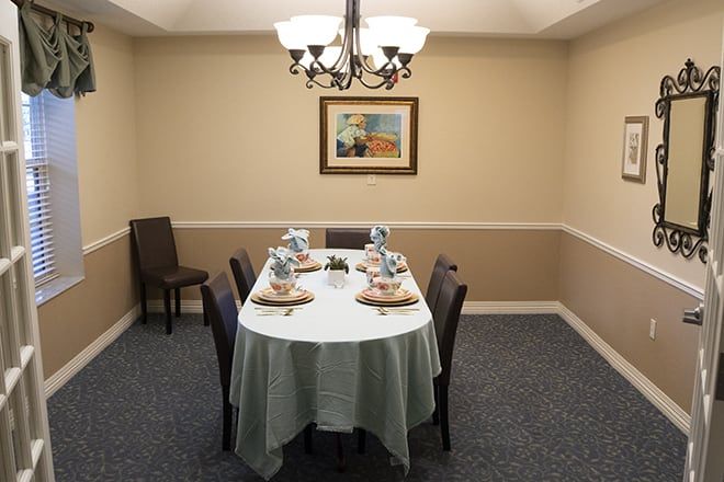 A neatly set dining table with a chandelier overhead and artwork on the wall.