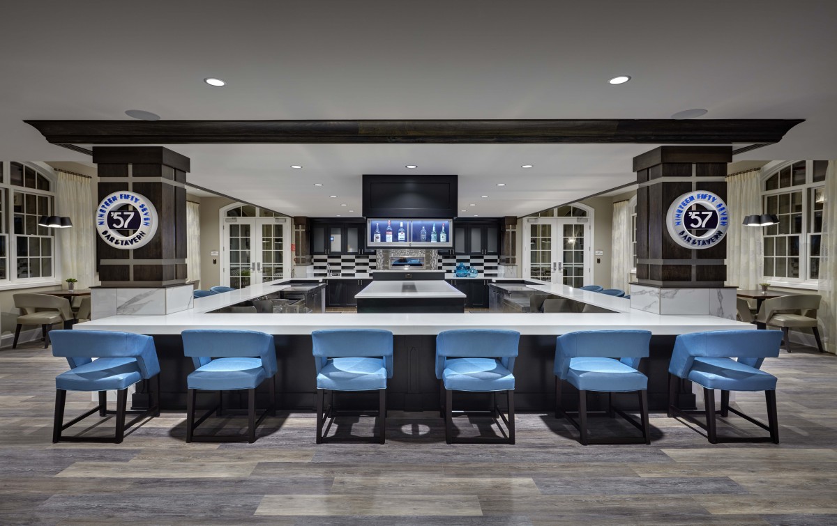 A modern kitchen with a large central island and blue bar stools under ambient lighting.