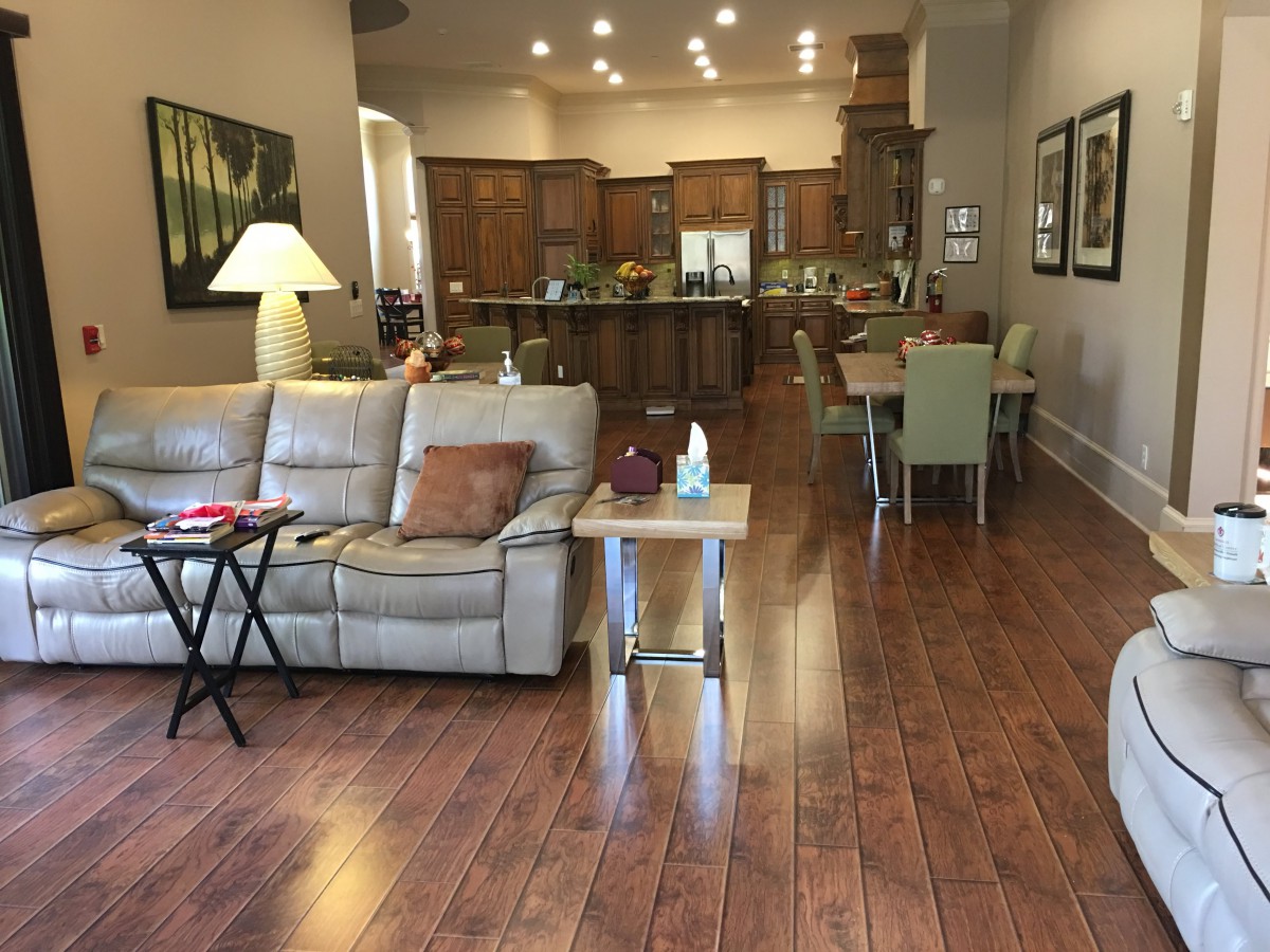 A spacious living room with an open floor plan leading to a kitchen and dining area, featuring wood flooring and comfortable seating.