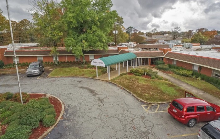A brick building with a green awning and adjacent parking lot under a cloudy sky.