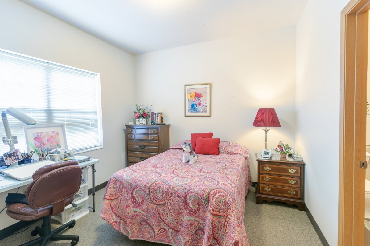 A cozy bedroom with a pink bedspread, red lamp, and wooden furniture.