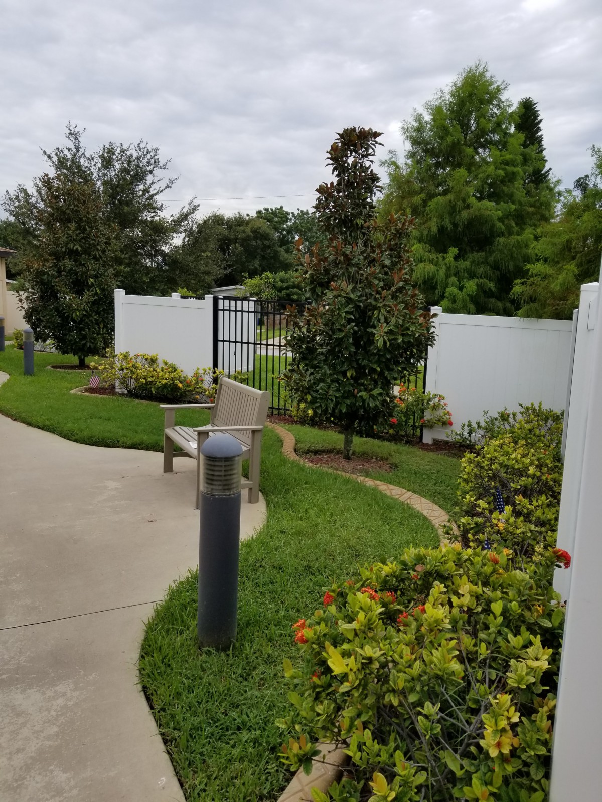A landscaped garden pathway with a white fence, surrounded by lush greenery and plants.