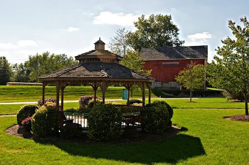 A picturesque view of a gazebo surrounded by lush greenery and a charming building in the background.