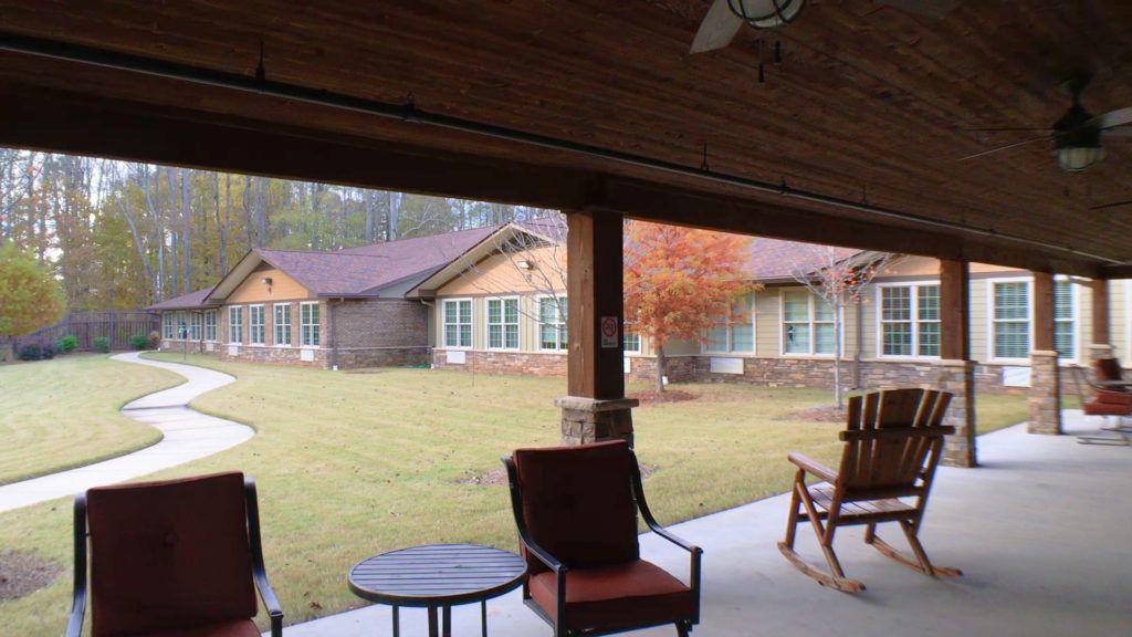 A cozy patio with rocking chairs and a table overlooking a well-maintained lawn and building.
