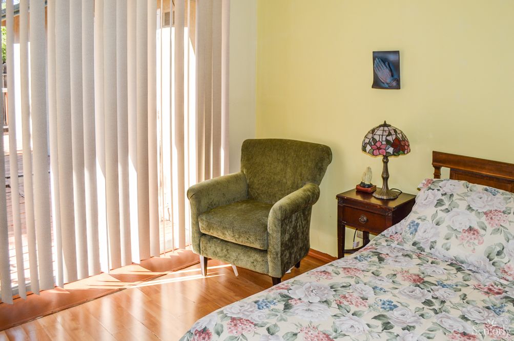A cozy bedroom corner with a green armchair, floral bedspread, and a stained glass lamp on a wooden side table.