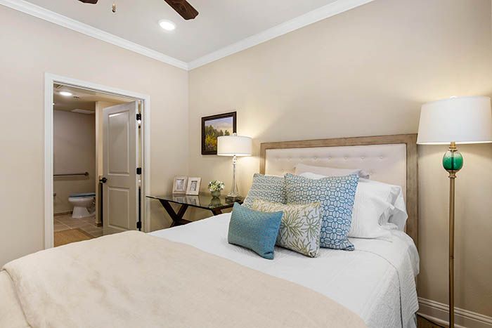 A cozy bedroom with a neatly made bed adorned with decorative pillows, a lamp, and framed pictures on a side table.