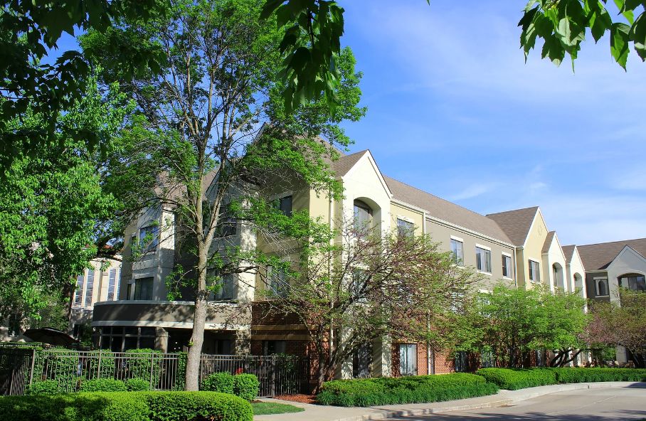 A residential apartment building surrounded by lush greenery and trees on a sunny day.