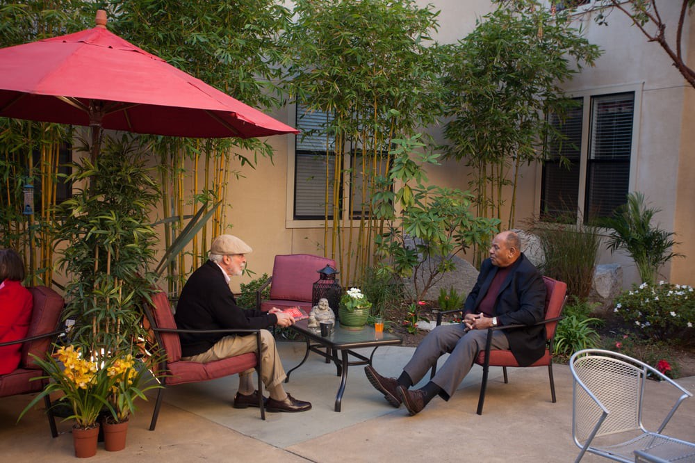 Two people sit in a garden patio having a conversation.