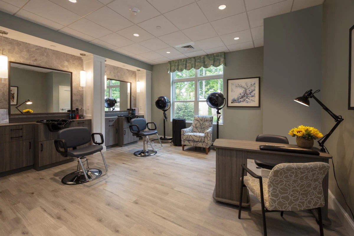 A cozy salon interior with styling chairs, mirrors, and hair dryers, set against a large window.