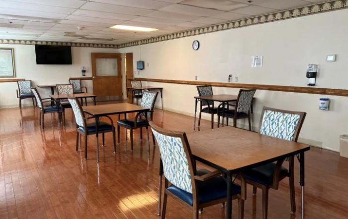 An empty dining room with multiple tables and chairs arranged neatly on a wooden floor.