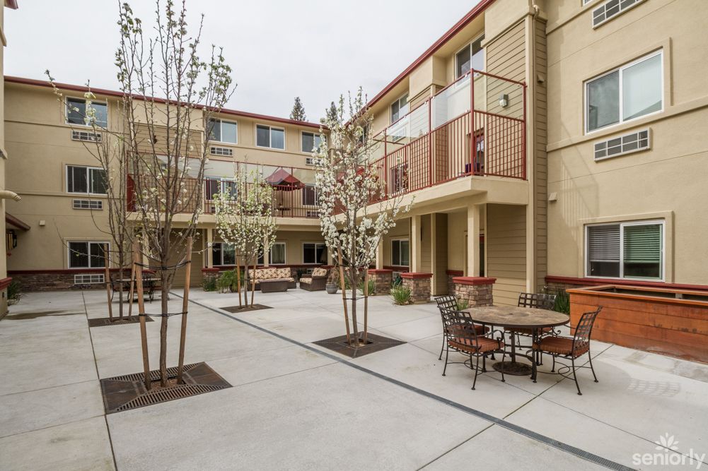 A view of an apartment complex courtyard with outdoor seating and young trees.