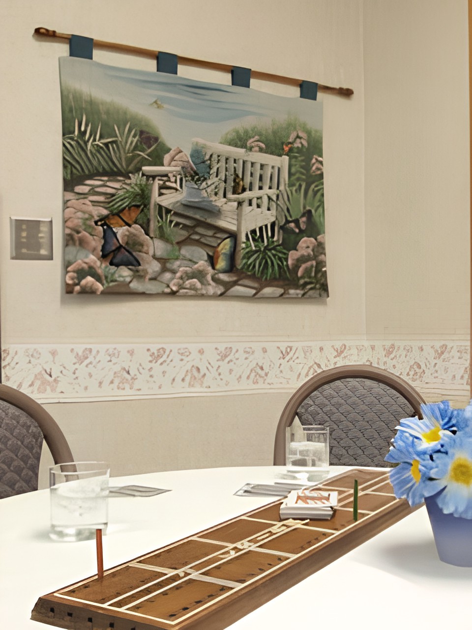 A dining area with a decorated table, featuring a floral centerpiece and wall art depicting a garden scene.