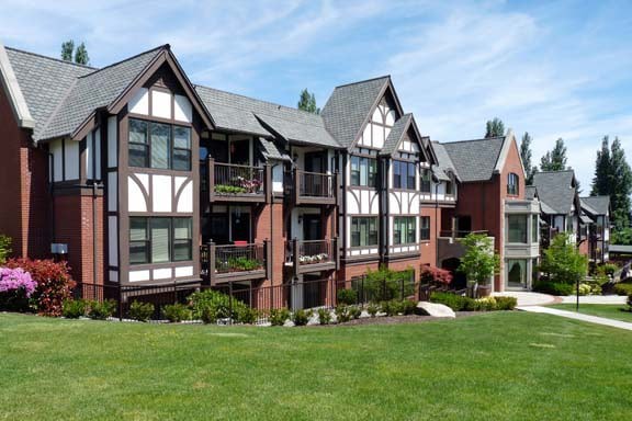 A Tudor-style residential apartment building with a well-maintained lawn in front, under a clear blue sky.