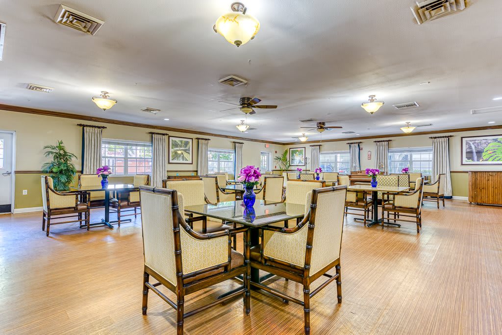 A well-lit dining area with neatly arranged tables and chairs, adorned with flowers.