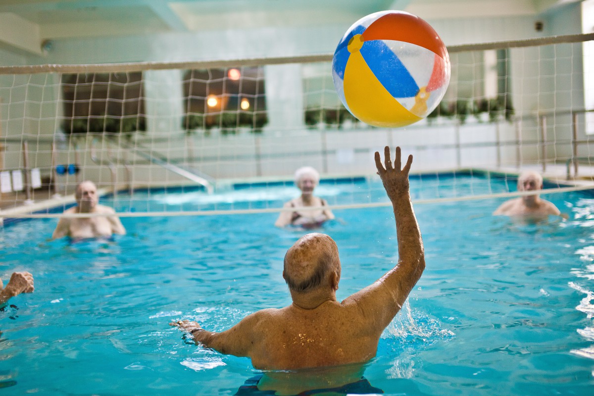 Elderly individuals enjoying a fun game with a beach ball in an indoor swimming pool.