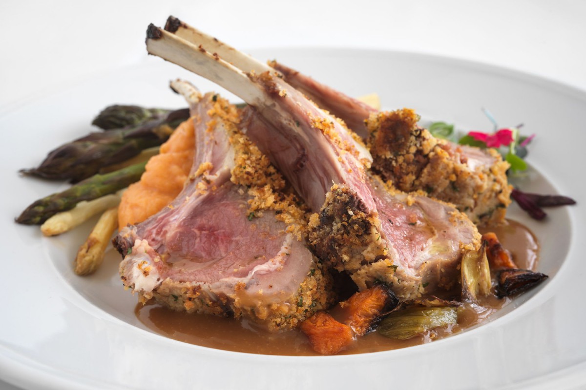 A gourmet plate featuring a rack of lamb served with vegetables.