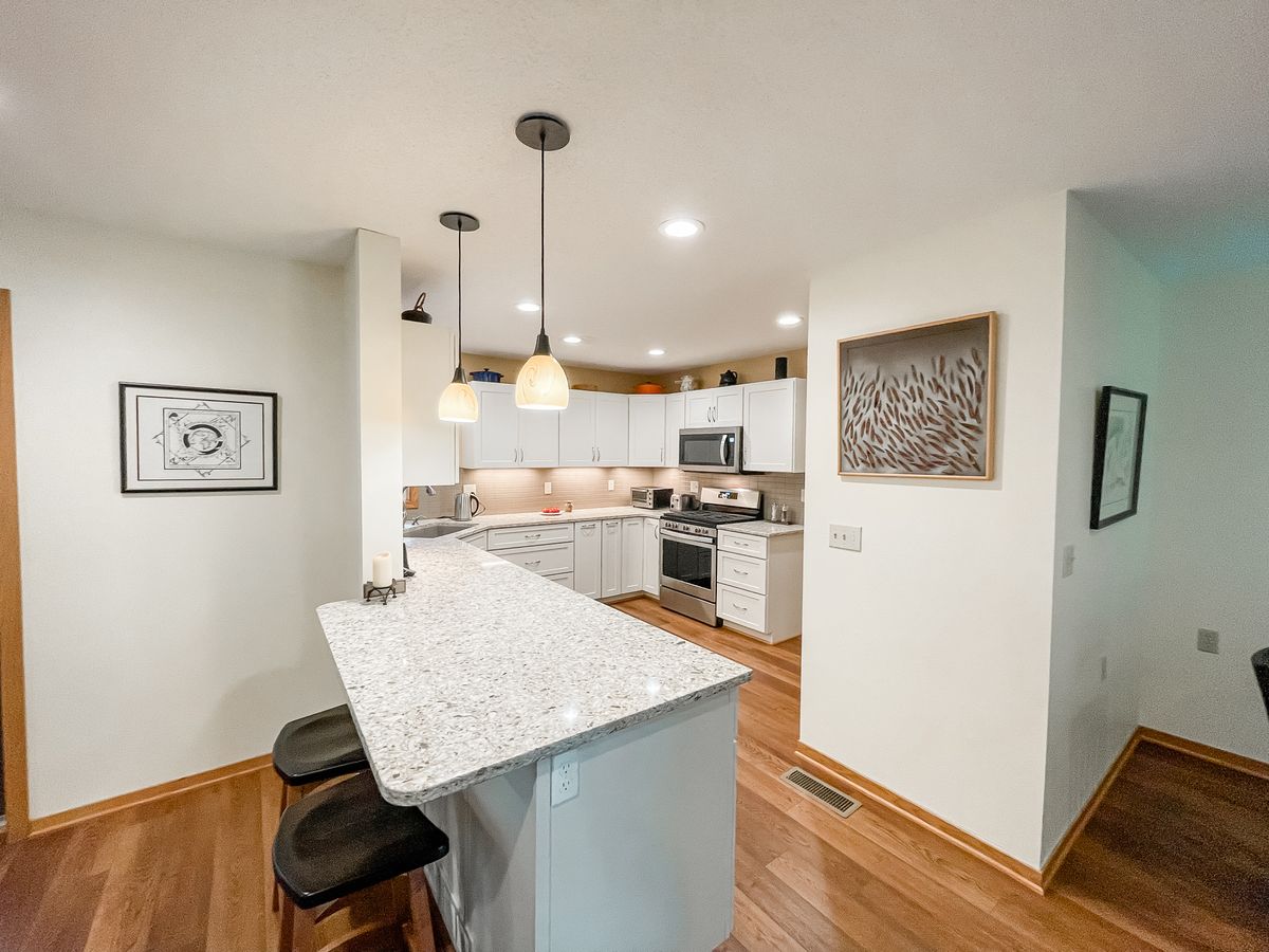 A modern kitchen featuring white cabinets, granite countertops, and an island with bar stools.