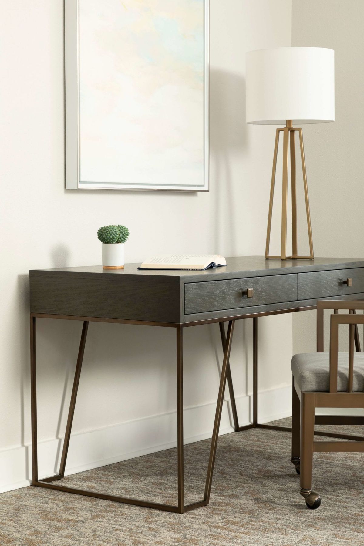 A minimalist home office setup featuring a dark wooden desk with two drawers, complemented by a modern lamp and small potted plant.