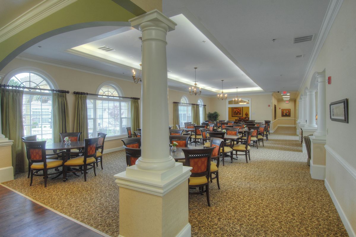 A spacious and well-lit dining area furnished with multiple tables and chairs, featuring carpeted flooring and ceiling lights.