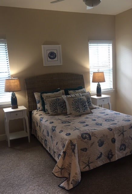 A cozy bedroom with a decorated bed, nightstands, and lamps near two windows.