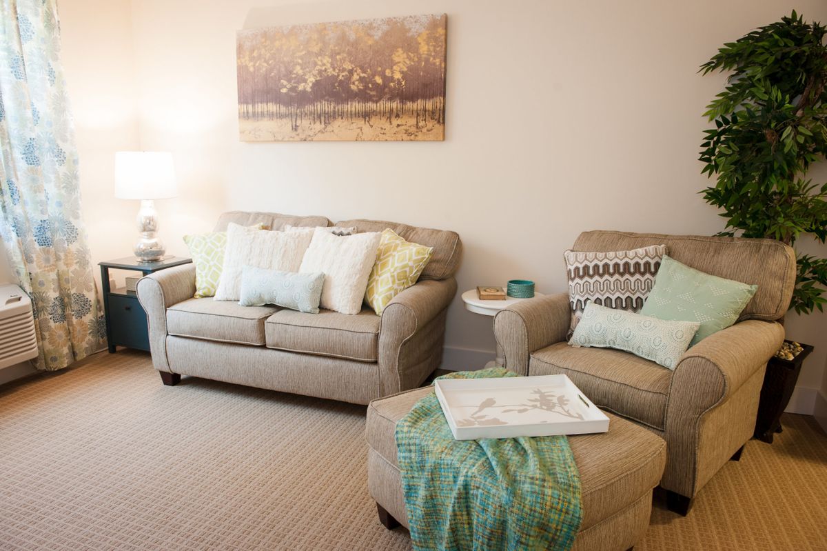 A cozy living room with a beige sofa and armchair, adorned with soft cushions and a decorative painting on the wall.