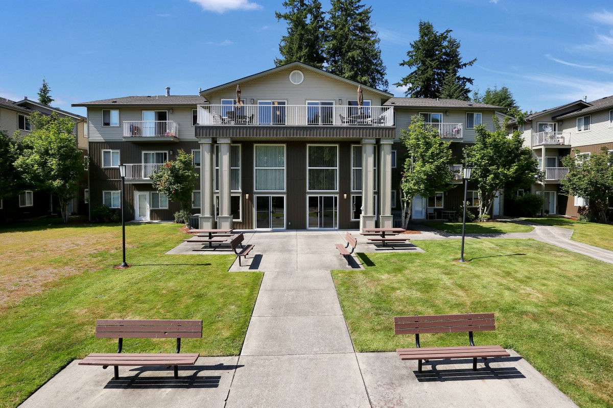A residential apartment building with a well-maintained lawn and benches in front.