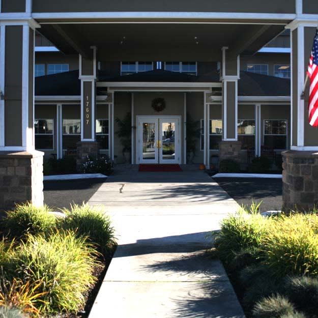 A welcoming entrance to a building with landscaped greenery and an American flag.