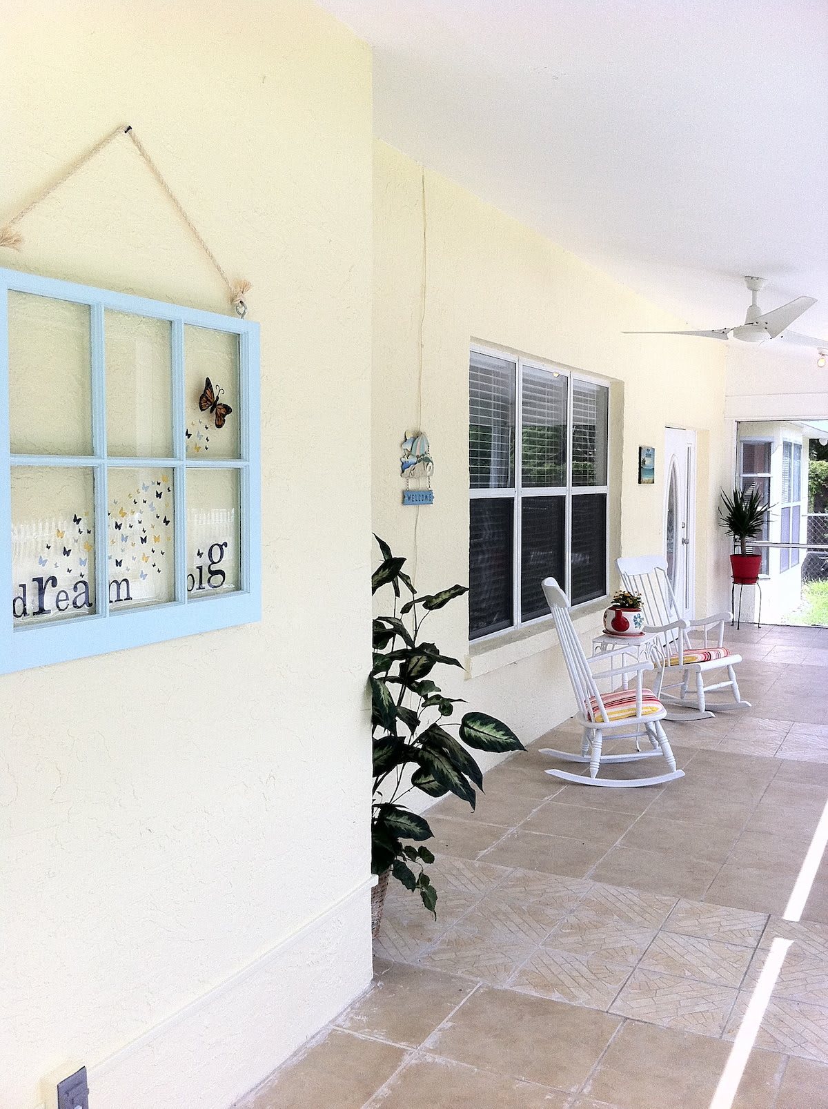 A bright and inviting porch with rocking chairs, wall decor, and large windows.