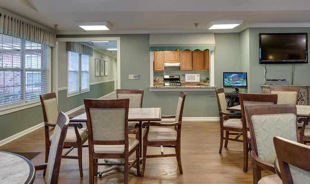 A cozy dining area with several tables and chairs, adjacent to a kitchen and computer station.