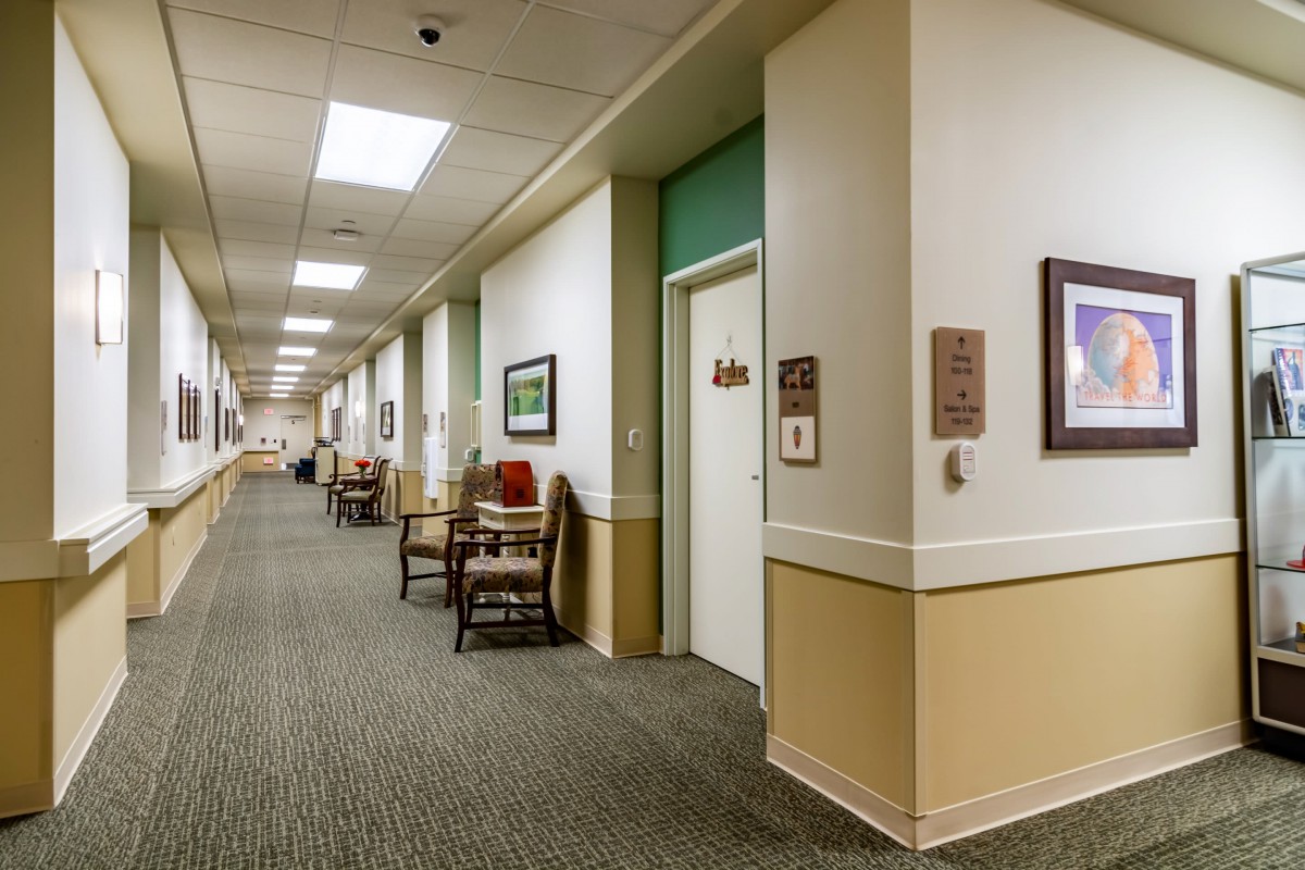 A brightly lit hallway with several chairs and doors along the corridor.