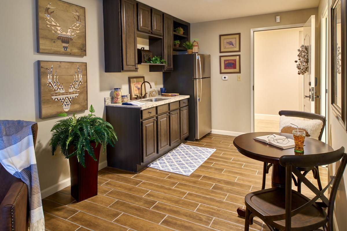 A cozy kitchen and dining area with wooden cabinets, a small fridge, and a potted plant.