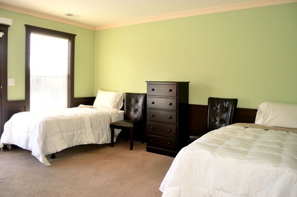 A cozy bedroom with two twin beds, a dresser, and two chairs against light green walls.