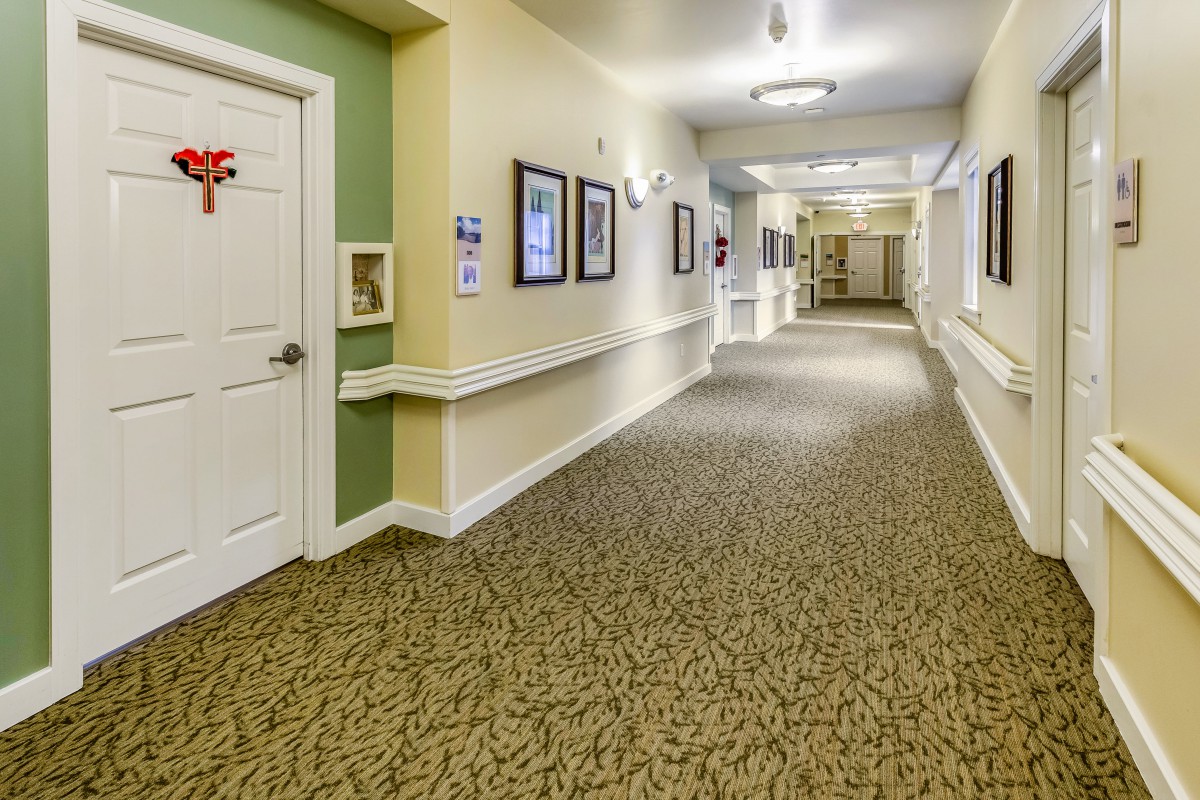 A well-lit interior hallway with carpeted flooring, decorated walls, and several doors.