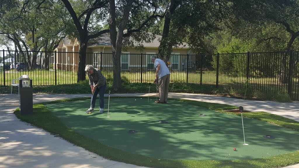 Two men playing on a putting green surrounded by trees.