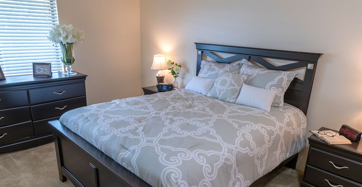 A neatly made bed with patterned bedding next to a nightstand with a lamp and decor.