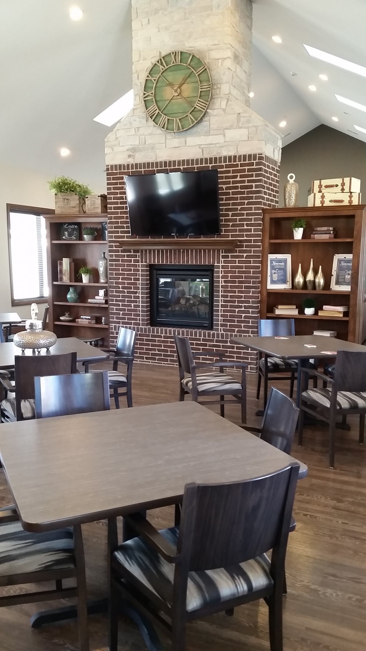 A cozy dining area with a brick fireplace and a television, surrounded by tables and chairs.