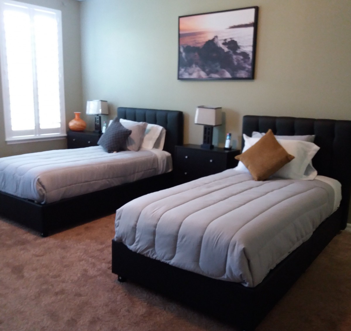 A well-decorated bedroom with two twin beds, bedside tables, lamps, and a landscape painting above the beds.