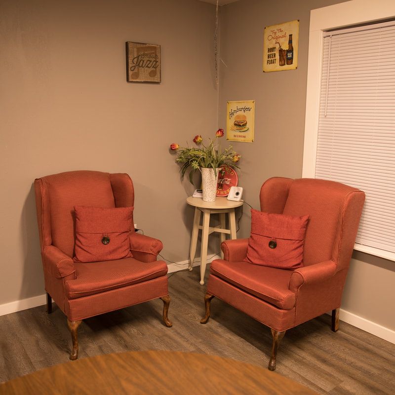 A cozy living room corner with two red chairs, a side table adorned with flowers, and wall art.