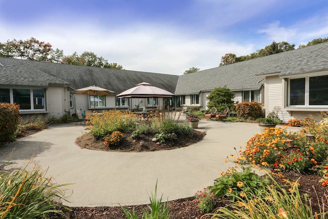 A scenic garden courtyard with vibrant plants and flowers surrounding a patio area at the back of a house.
