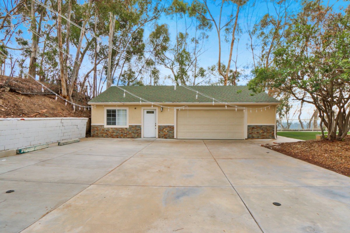 A single-story house with a spacious driveway surrounded by tall trees.