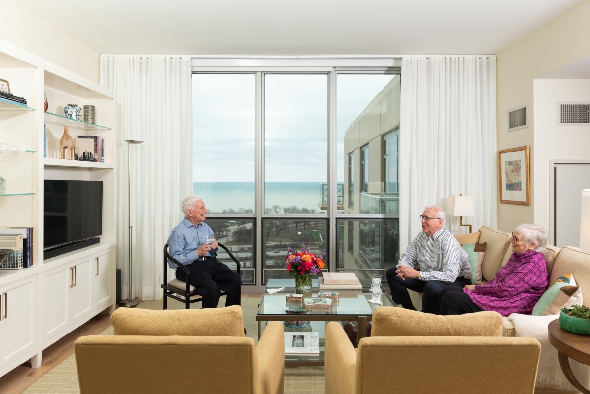Two people engaged in conversation in a bright living room with a window view.